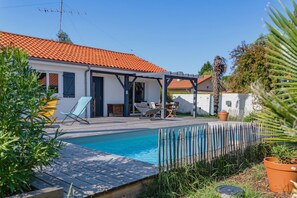 Een woonhuis met een zwembad, tuinmeubilair en een overdekt terras.