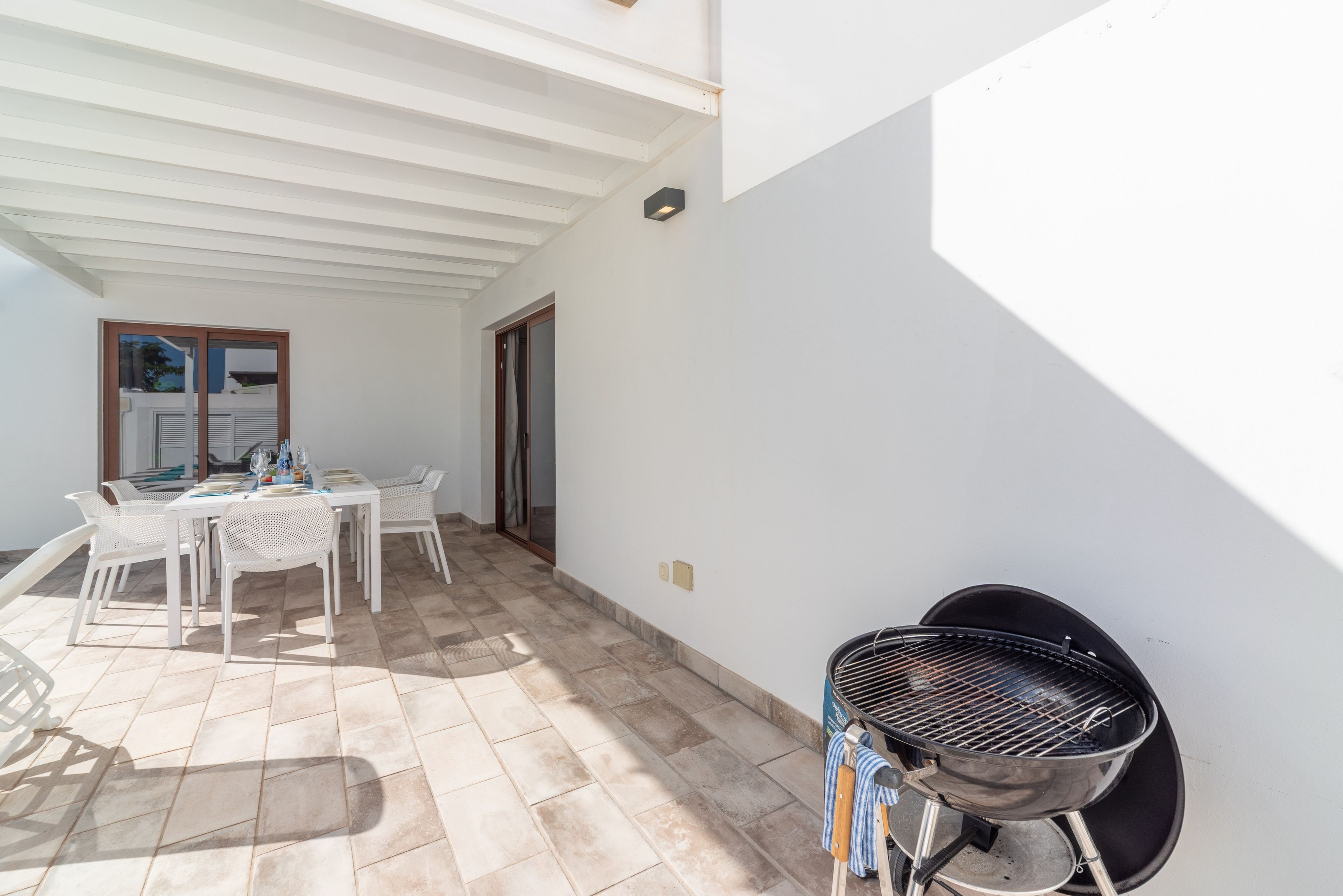 Eine Terrasse im Freien mit einem Esstisch, Stühlen, einem Grill und einer Tür zu einem anderen Raum.