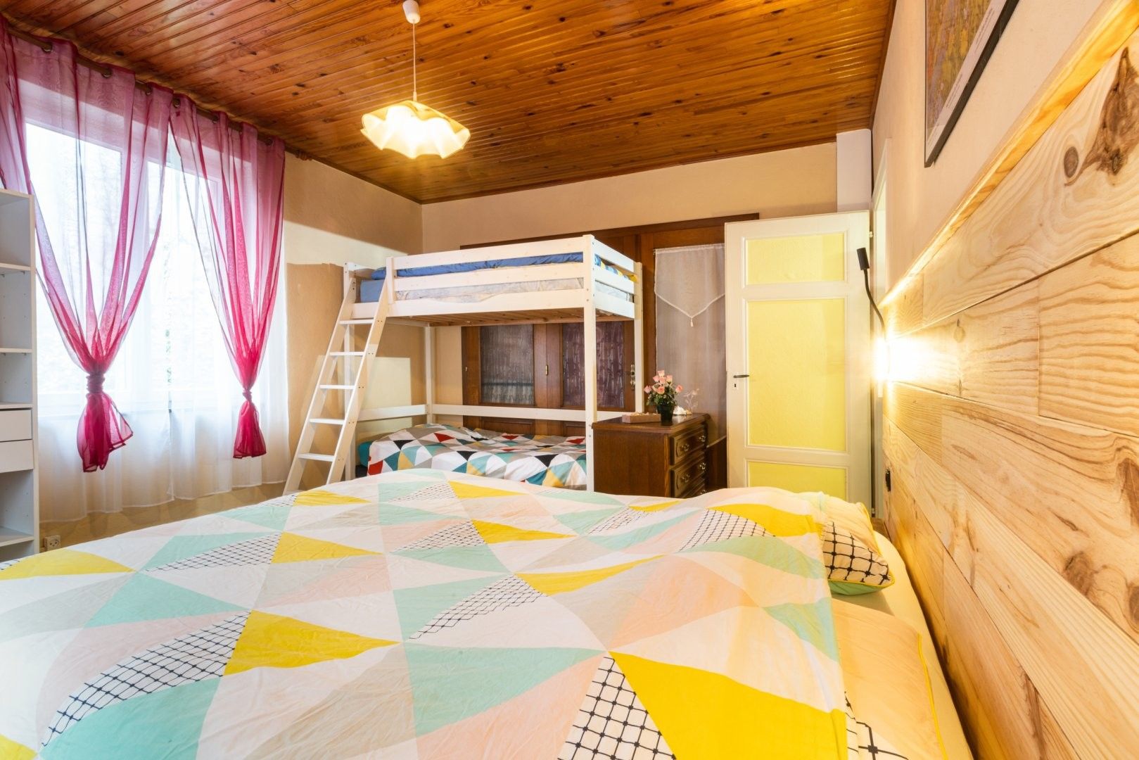 A bedroom with a bunk bed, a ladder, a wooden headboard, and a quilted bedspread.