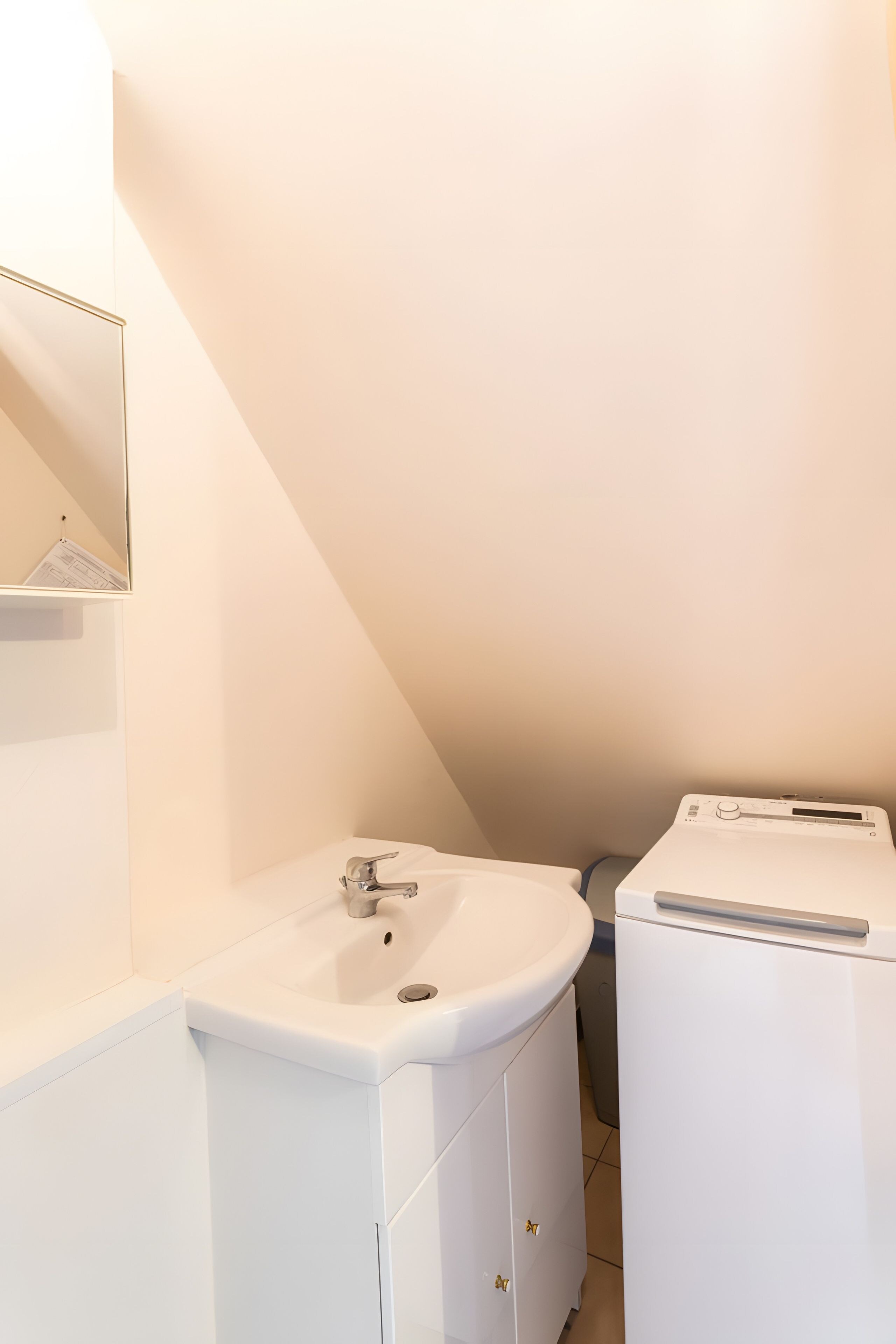 A small, white bathroom with a sink, a mirror, and a washing machine.