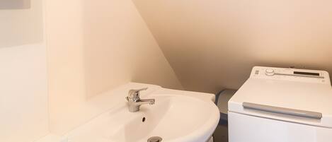 A small, white bathroom with a sink, a mirror, and a washing machine.