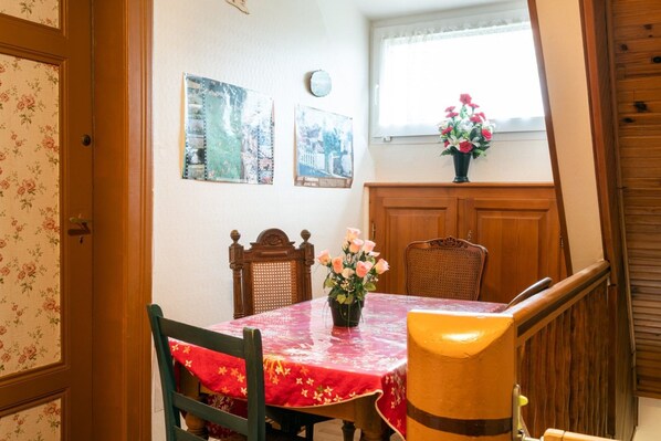 A dining area with a table set for two, a vase of flowers, and a window with a view. - Gîte “Gîtes du Niederwald” with Shared Terrace, Wi-Fi, and Air Conditioning (Guémar)