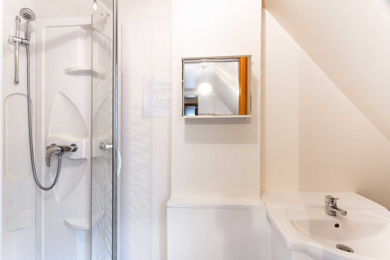 A bathroom with a glass shower enclosure, a sink, and a mirror.