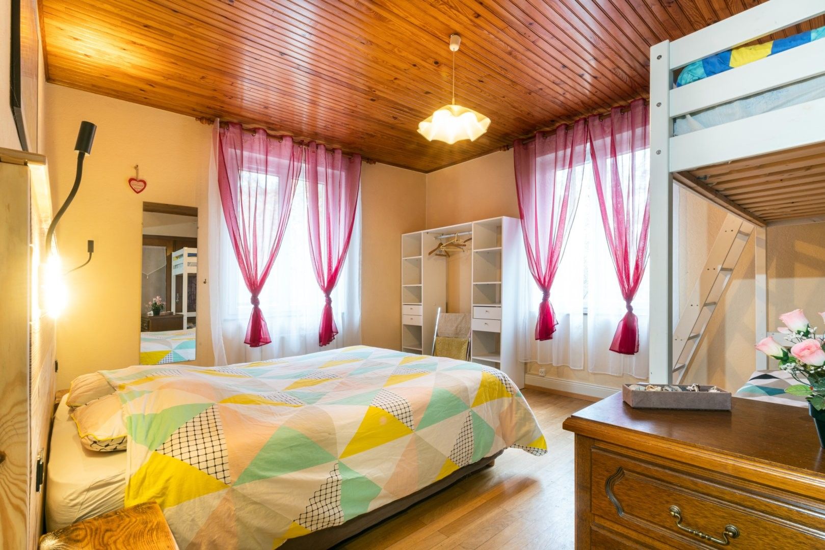 A bedroom with a bed, a dresser, a wardrobe, and a mirror.