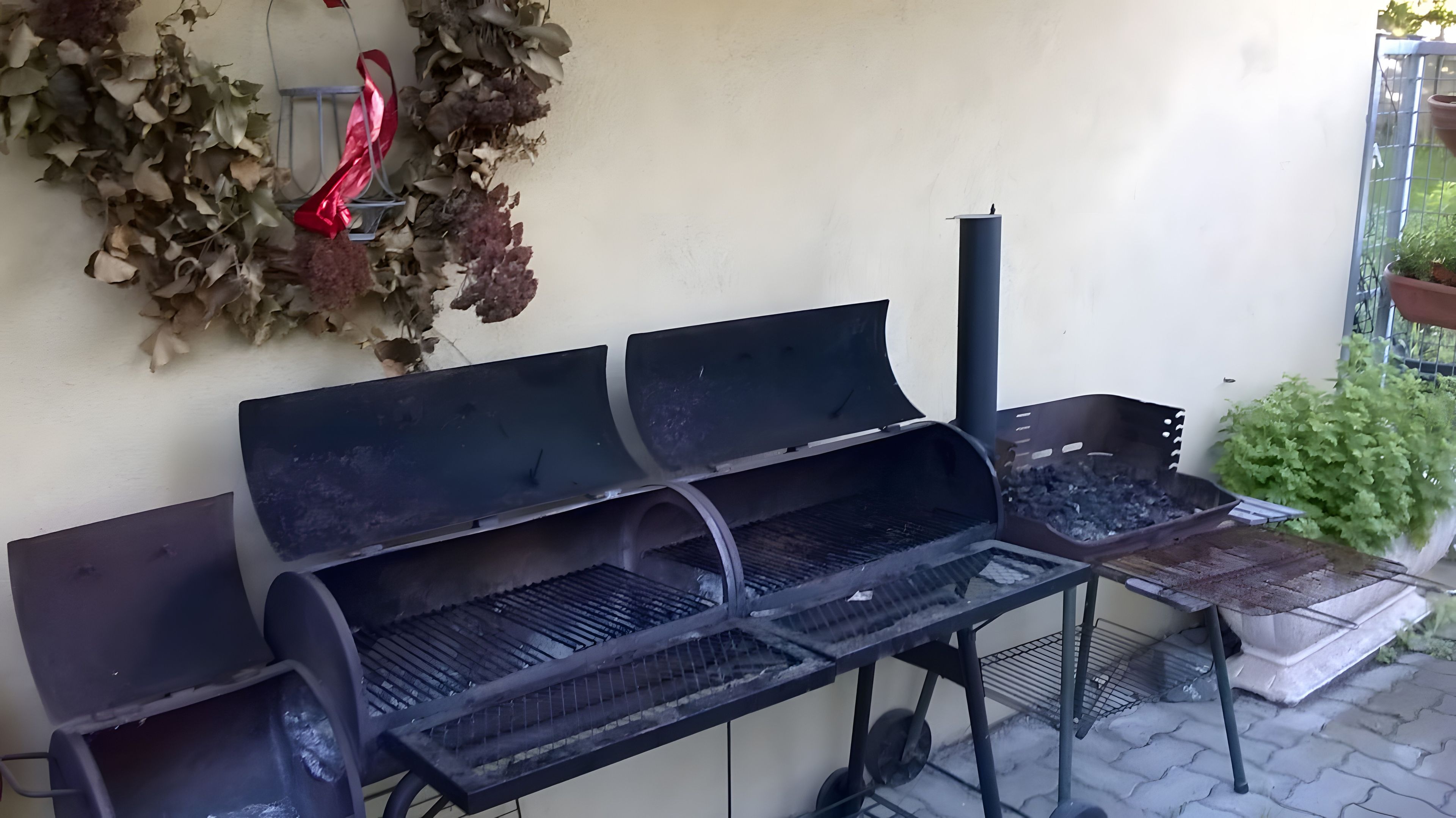 An outdoor grill with a metal frame, a chimney, and a wall-mounted decorative wreath.