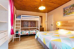 Une chambre avec un lit superposé, une échelle, un bureau et un lit recouvert d’une couverture aux couleurs vives.