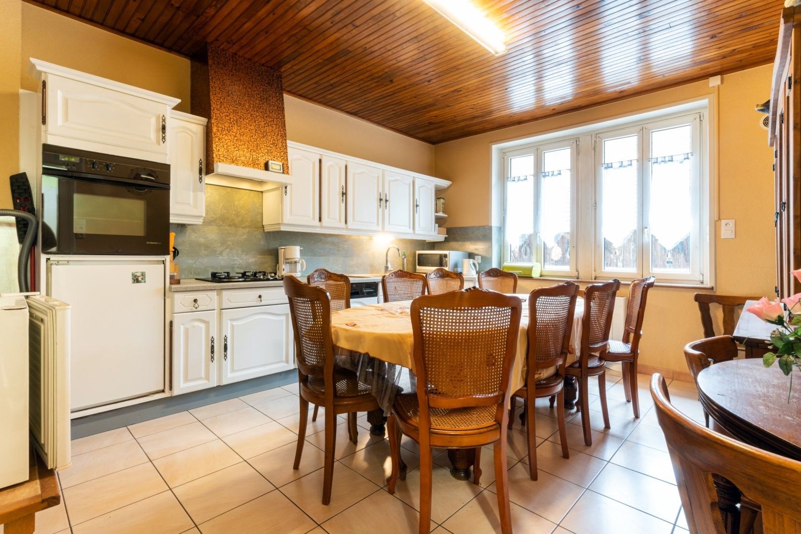 Une cuisine avec des meubles blancs, un fourneau et un coin repas comprenant des chaises en bois et une table ronde.