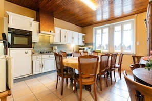 Une cuisine avec des meubles blancs, un fourneau et un coin repas comprenant des chaises en bois et une table ronde.