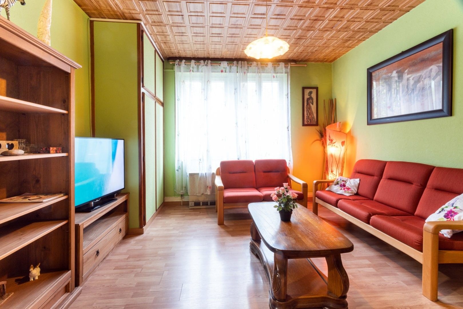 Una sala de estar con televisor, sofás rojos, estanterías de madera y una mesa de centro de madera.