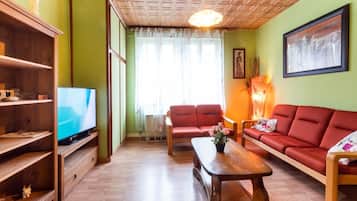 Una sala de estar con televisor, sofás rojos, estanterías de madera y una mesa de centro de madera.