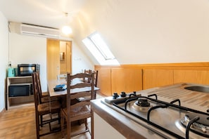Cocina compacta con estufa a gas, sillas de madera, mesa de comedor y microondas integrado.