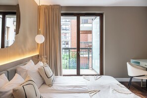 A modern bedroom with a large bed, a desk, and a view of a brick building through a sliding door. - Szafarnia in Gdańsk Old Town&Marina View (Gdańsk)