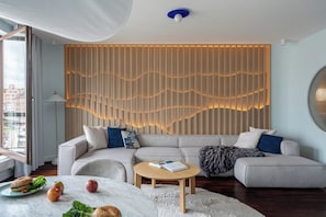 A modern living room with a sectional sofa, a round coffee table, and a decorative wall panel. - Szafarnia in Gdańsk Old Town&Marina View (Gdańsk)