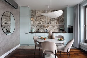 A modern kitchen with marble backsplash, light blue cabinets, and a dining area with a round table and chairs. - Szafarnia in Gdańsk Old Town&Marina View (Gdańsk)