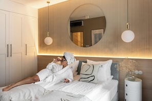 A modern bedroom with a bed, a bedside table, a mirror, and a wall-mounted light fixture. - Szafarnia in Gdańsk Old Town&Marina View (Gdańsk)