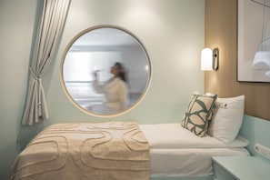A hotel room with a round mirror, a bed with a beige cover, a pillow with a leaf pattern, a nightstand, and a wall-mounted light fixture. - Szafarnia in Gdańsk Old Town&Marina View (Gdańsk)