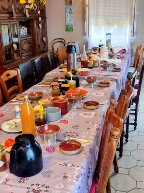 Une table à manger dressée avec différents plats, couverts et condiments, entourée de chaises en bois.