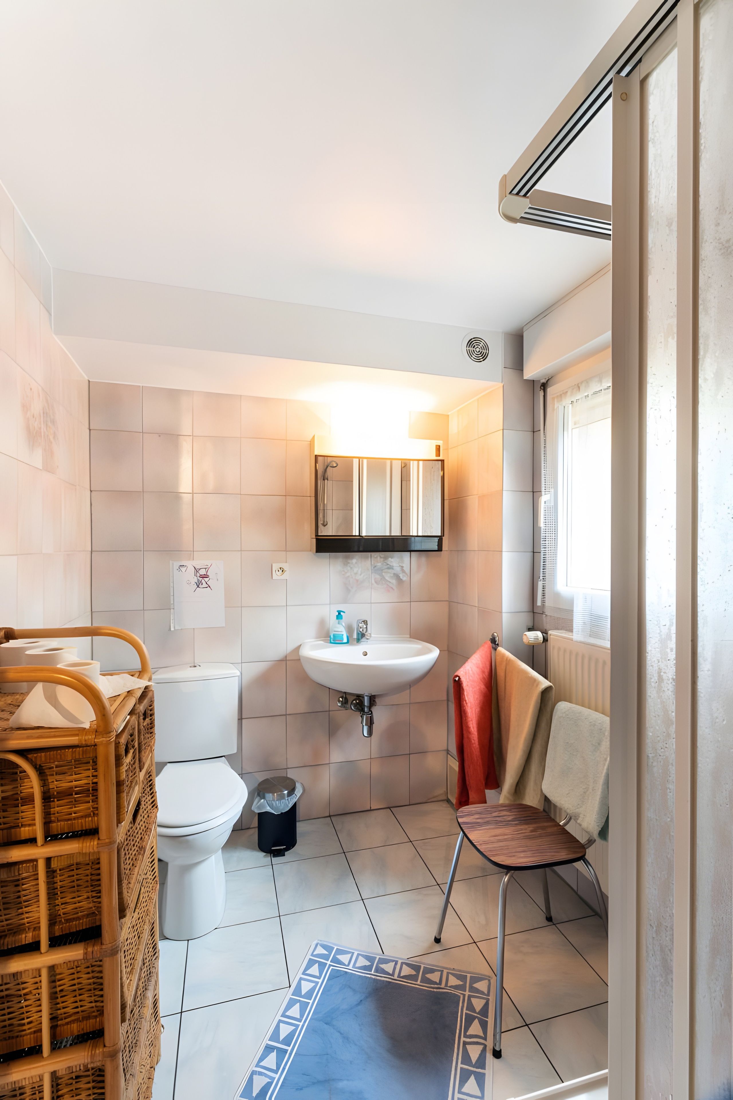 A bathroom with a toilet, sink, and a small chair.