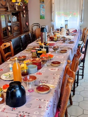 Une table à manger dressée avec différents plats, couverts et condiments, entourée de chaises en bois.