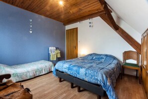 Une chambre avec deux lits, un plafond en bois, une chaise en bois et un petit tapis.