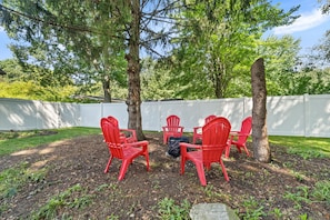 A patio area with red chairs arranged around a table, surrounded by trees and a white fence. - New Listing! Fenced Yard | Near Golf & Saugatuck (Saugatuck)