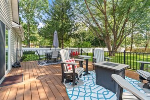 Eine Holzterrasse mit Gartenmöbeln, darunter Stühle und ein Tisch, sowie ein kleiner, integrierter Grill.