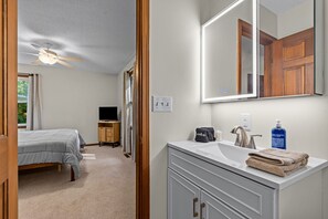 Ein Schlafzimmer mit einem Bett, einem Fernseher, einem Schminktisch und einem Badezimmer mit Waschbecken und Spiegel.