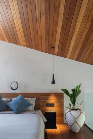 A modern bedroom with a wooden ceiling, a bed with blue and white bedding, a bedside table with a lamp, and a potted plant.