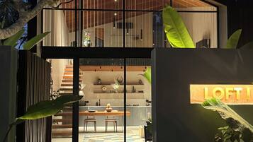Een modern huis met twee verdiepingen, een glazen gevel, een zichtbare keuken en een eethoek.
