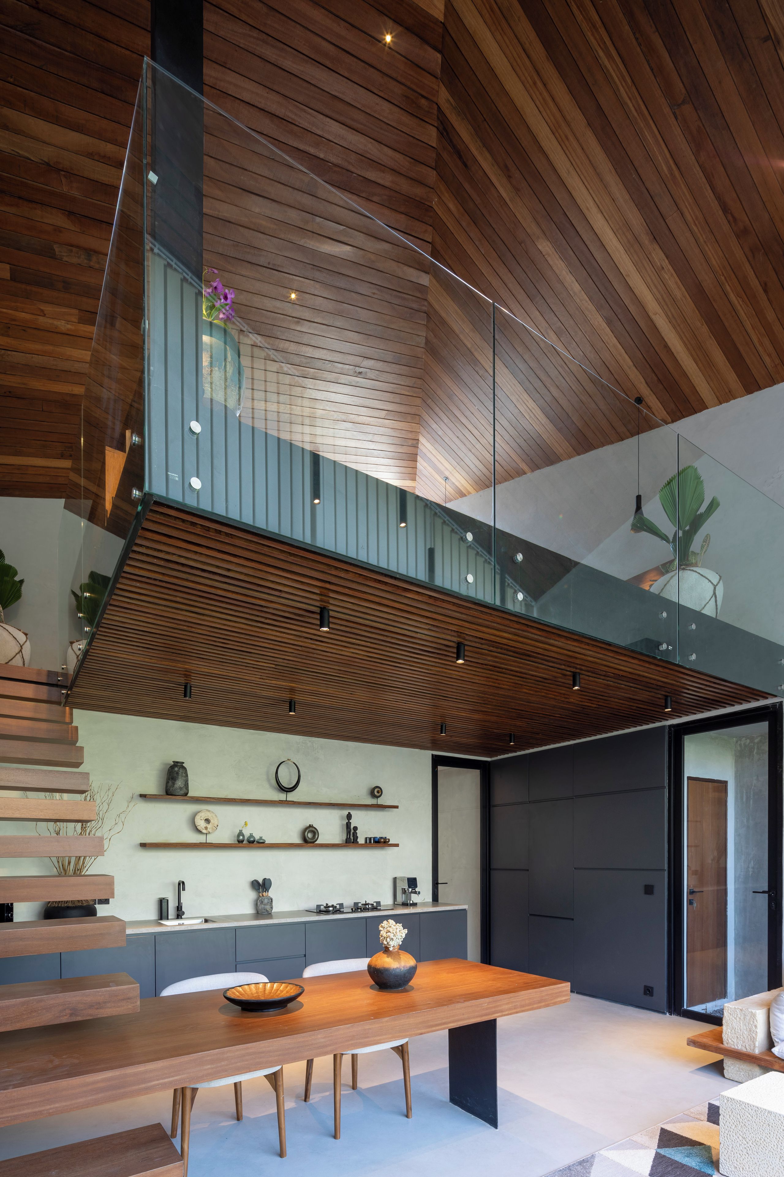 A modern kitchen with a wooden ceiling, a glass staircase, and a dining area with a wooden table.