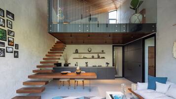 Ein modernes Interieur mit einer Treppe zu einem Erkerbereich, einem Esstisch mit Stühlen, einer Couch und einer Küche mit Regalen.