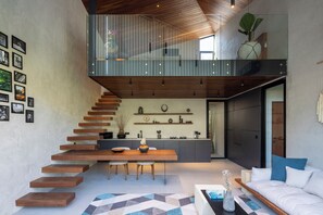 A modern interior with a staircase leading to a loft area, a dining table with chairs, a sofa, and a kitchen with shelves.
