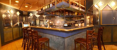 A bar area with a central counter, multiple stools, and shelves stocked with bottles.