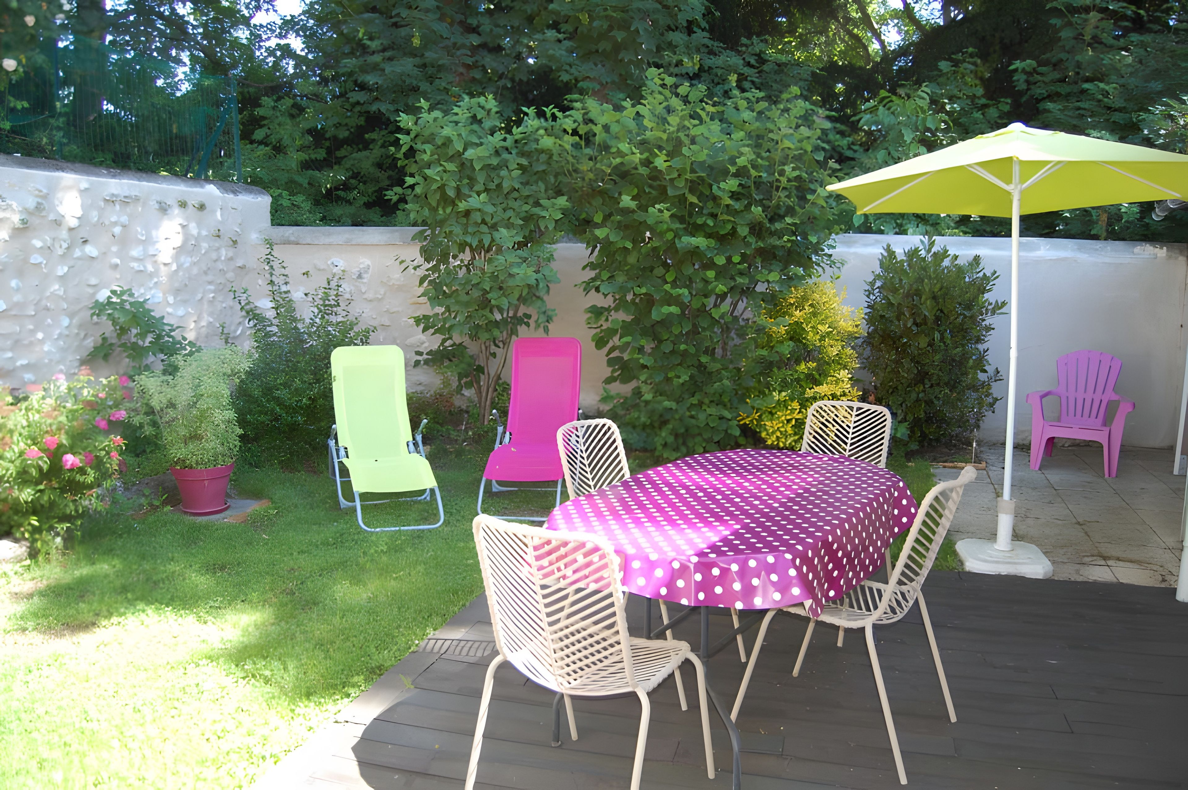 Patio esterno con tavolo e sedie, immerso nel verde e delimitato da un muro bianco.