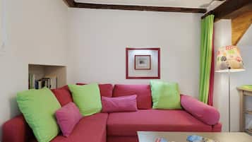 Ein Wohnzimmer mit einem roten Sofa, grünen und rosafarbenen Kissen, einem gerahmten Bild an der Wand und einem Tisch mit Zeitschriften.
