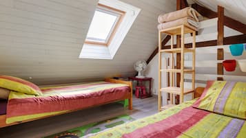 Een gezellig slaapkamer onder het dak met twee houten bedden, een dakraam, een ventilator en een stapelbed met opbergruimte.