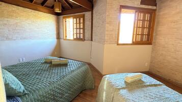 Una habitación con dos camas, una pared de ladrillo y una ventana con persianas de madera.