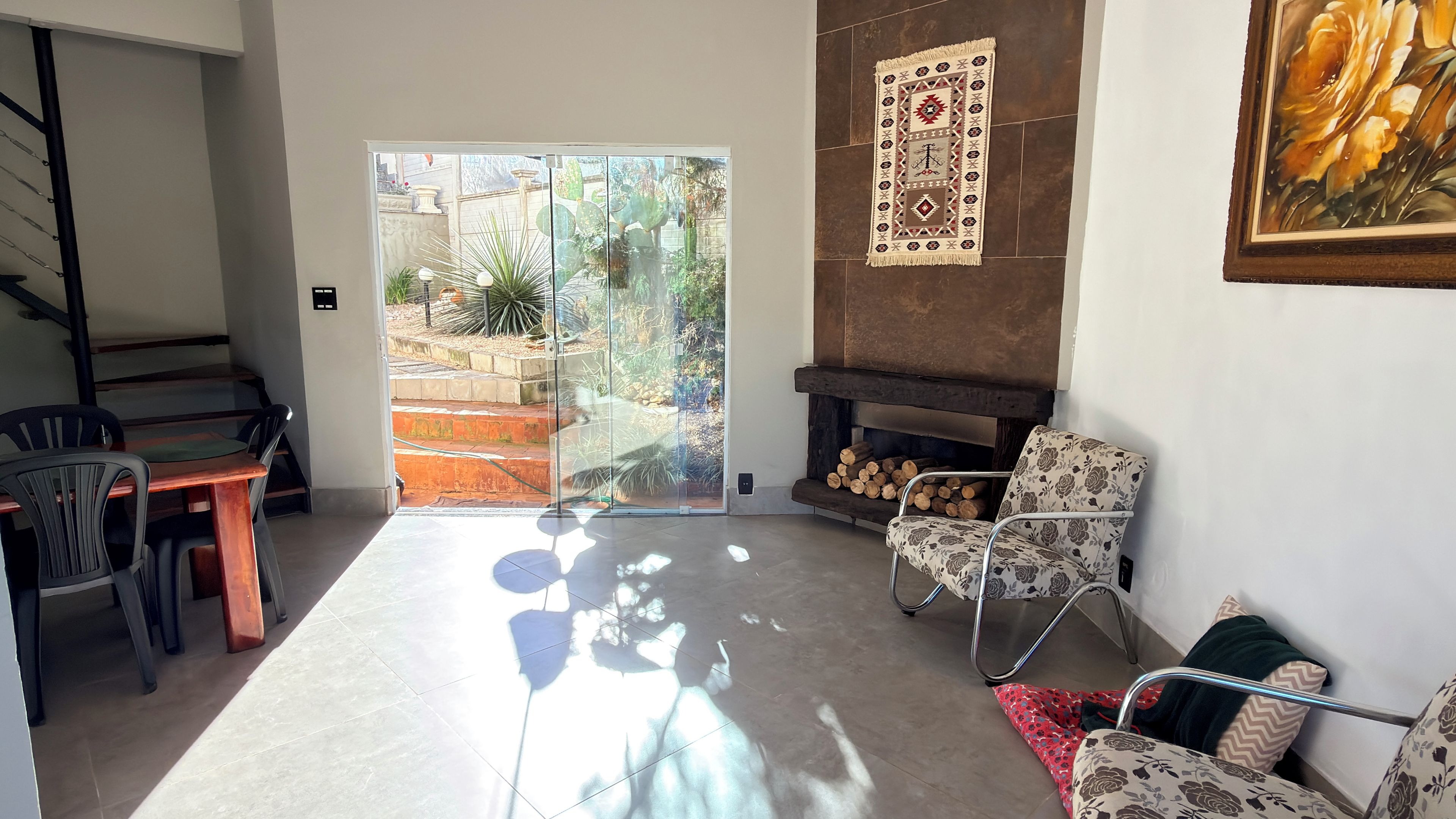 Una sala de estar con puerta de vidrio que da a un jardín, chimenea y comedor con sillas.