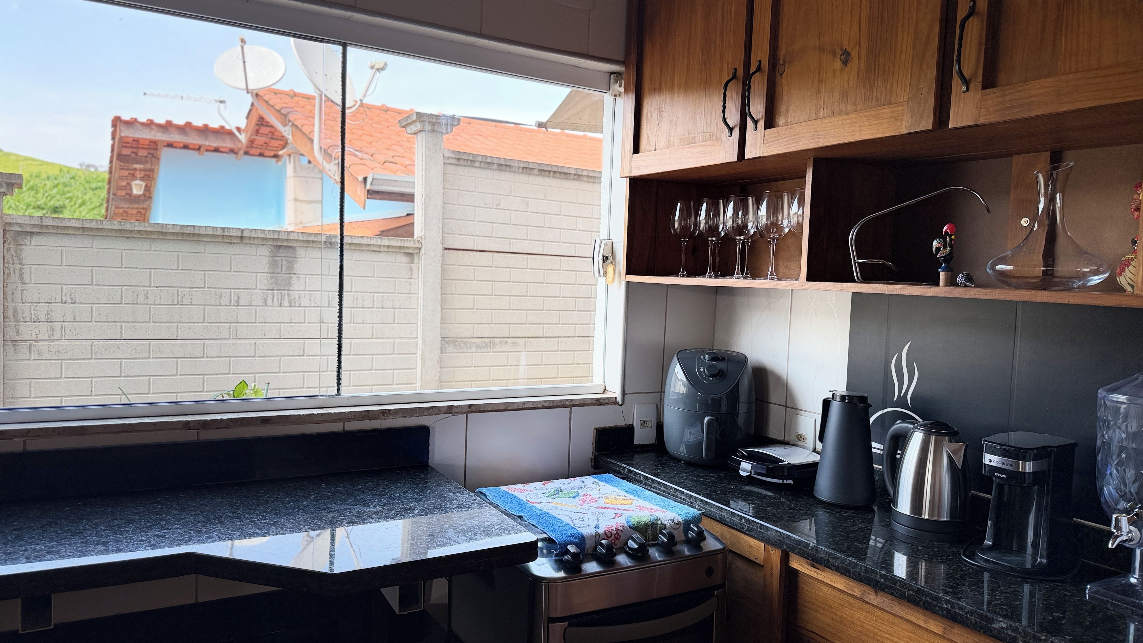 A kitchen with a window, a stove, a coffee maker, and a cabinet with glassware.