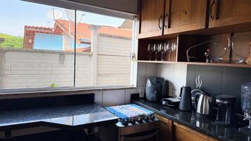 A kitchen with a window, a stove, a coffee maker, and a cabinet with glassware.