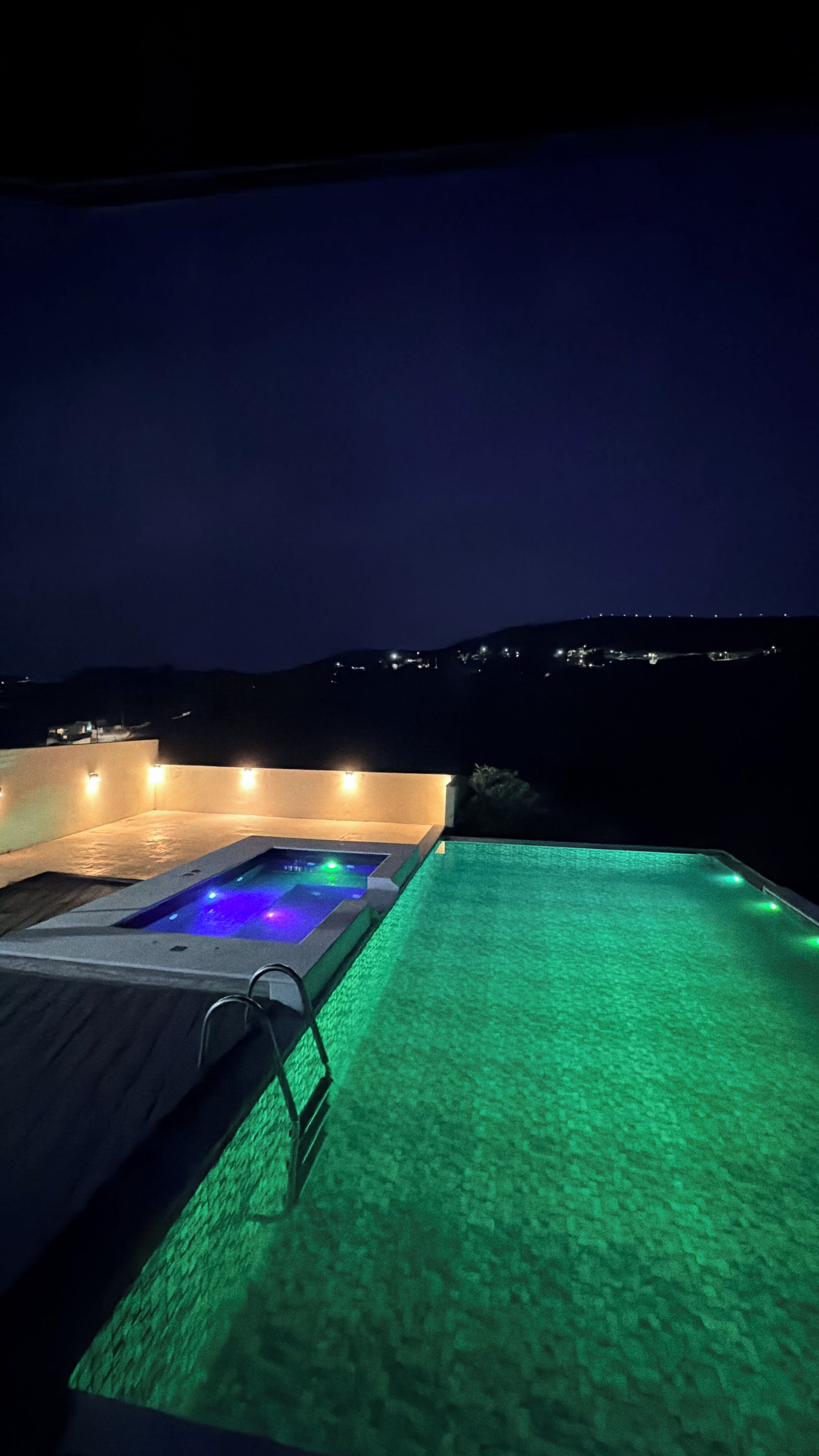 Piscina nocturna con hidromasaje y vistas a las colinas.