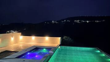 Piscina nocturna con hidromasaje y vistas a las colinas.
