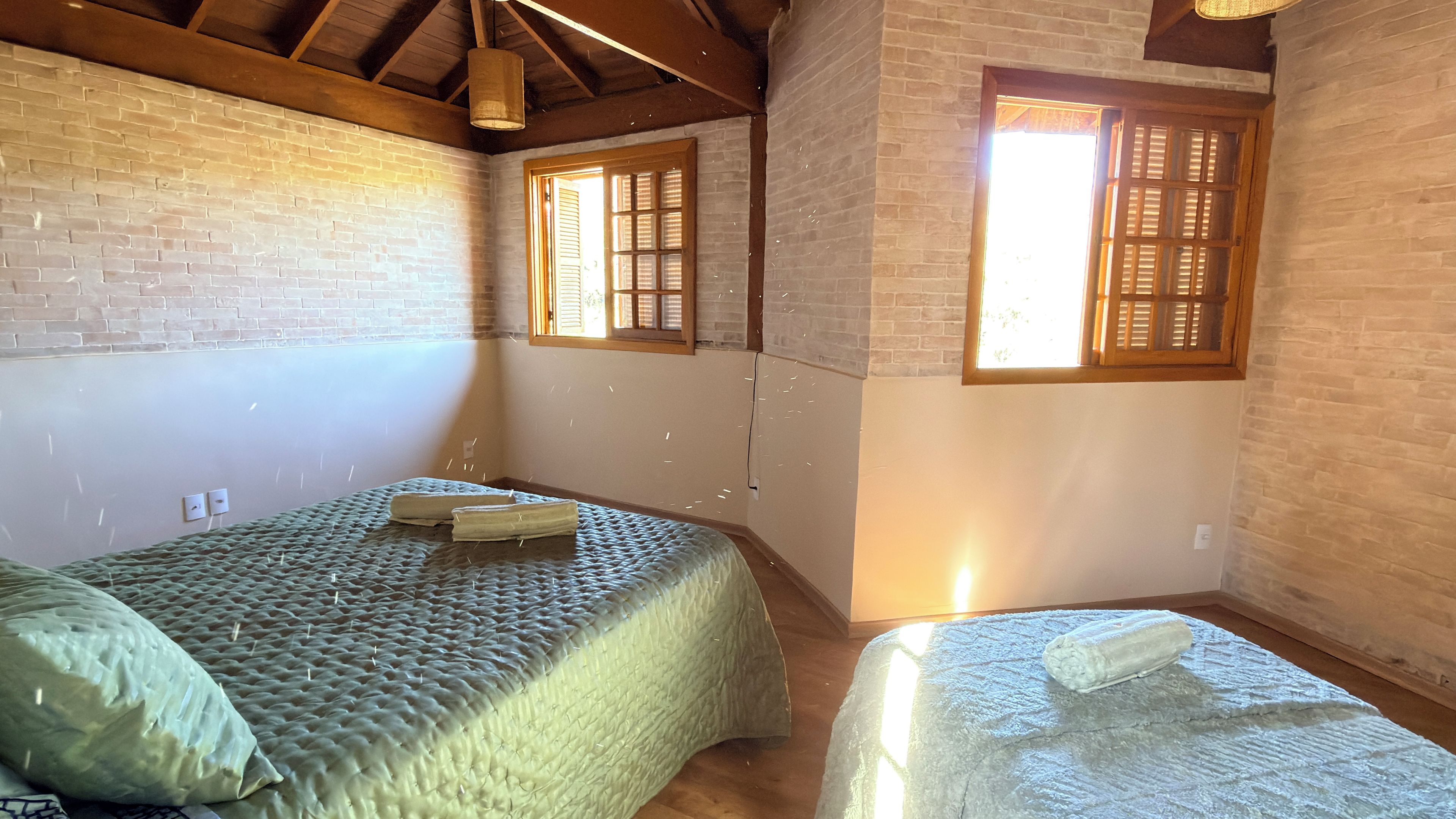 A room with two beds, a brick wall, wooden beams, and two windows with wooden shutters.