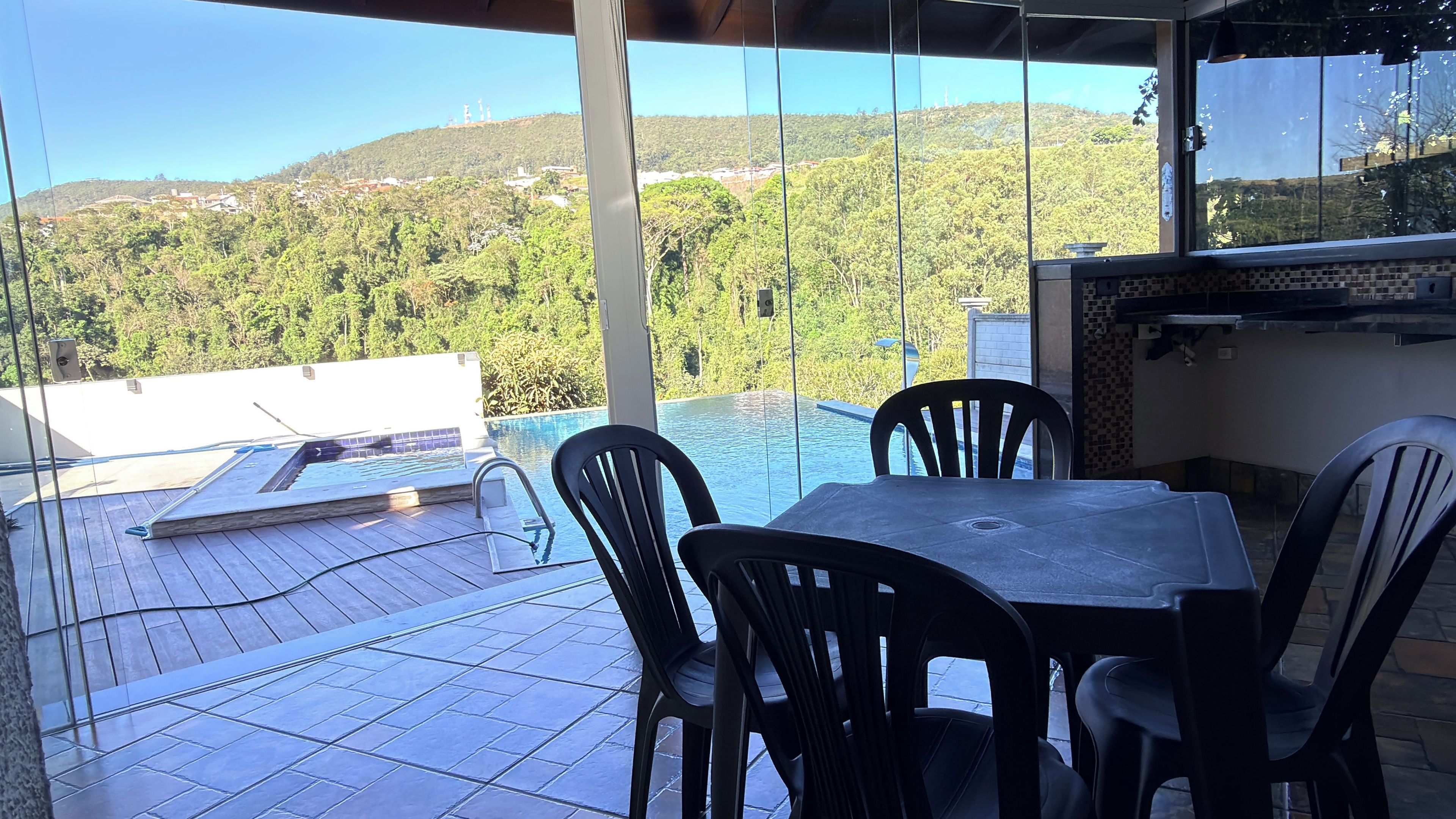 Eine Terrasse mit Pool, Stühlen und Tisch, mit Blick auf einen bewaldeten Hang.