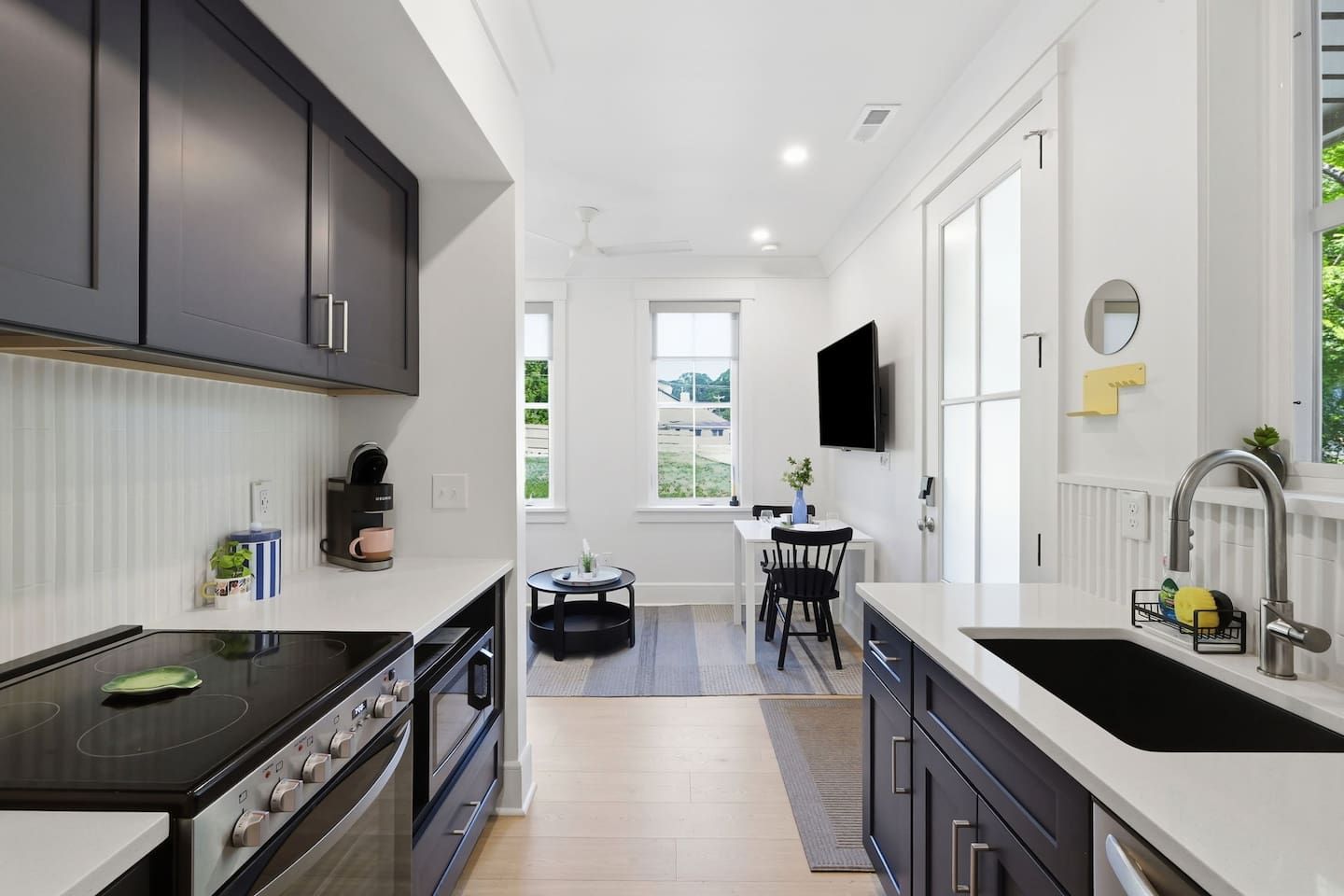 A modern kitchen with a stove, oven, and sink, a dining area with a table and chairs, and a TV mounted on the wall.