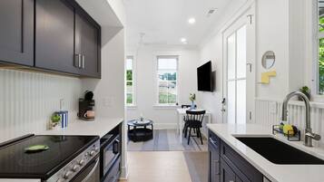 A modern kitchen with a stove, oven, and sink, a dining area with a table and chairs, and a TV mounted on the wall.