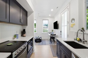 Cozinha moderna com fogão, forno e pia, área de refeições com mesa e cadeiras, e uma TV fixada na parede.