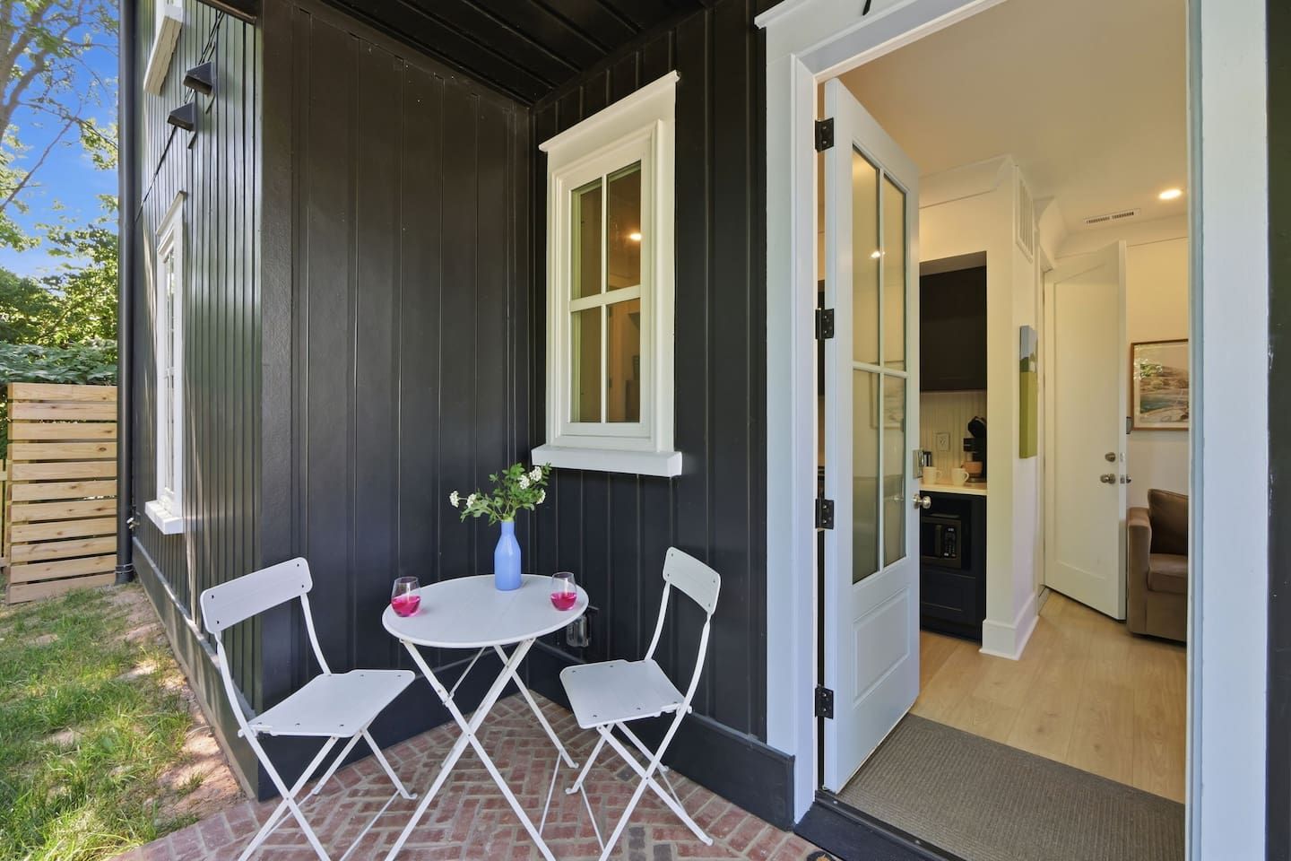 A patio with a table and chairs, a vase with flowers, and a door leading to a kitchen.