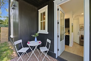 A patio with a table and chairs, a vase with flowers, and a door leading to a kitchen. - Downtown Centric, Tucked Away, Fenced, PetsOK (Durham)