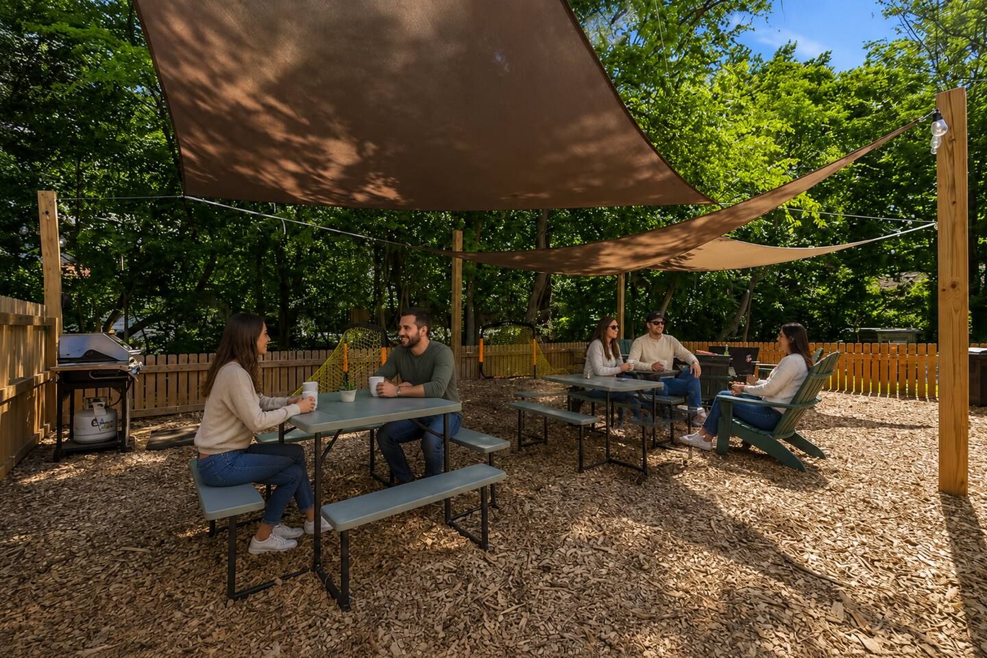 An outdoor seating area with tables and benches, surrounded by trees and a wooden fence.